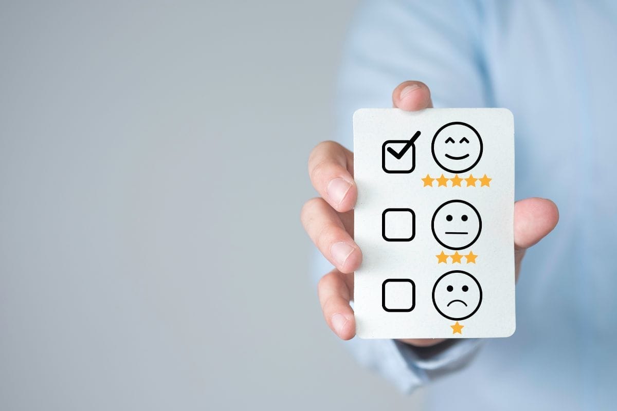 A person holding a card with a 5-star smiley face checked. The card also has space for a 3-star and a 1-star rating.